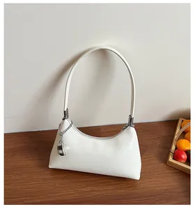 Detailansicht einer weißen Retro-Achseltasche mit silbernem Kettenanhänger auf Holz.