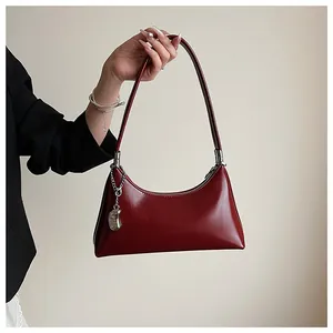 Detailansicht einer glänzenden weinroten Vintage-Achseltasche mit Metallanhänger.