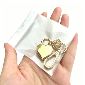 Detailaufnahme eines goldfarbenen Herzschloss-Schlüsselanhängers in einer Klarsichtverpackung.