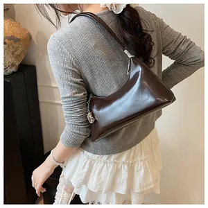Detailansicht einer retro dunkelbraunen glänzenden Achseltasche, getragen von einem Model.