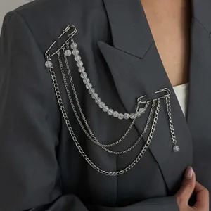 Broche à chaînes multi-rangs argentées avec perles transparentes sur blazer gris.