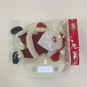 Close-up detail of a soft Santa Claus plush ornament being weighed at 13.6g on a digital scale