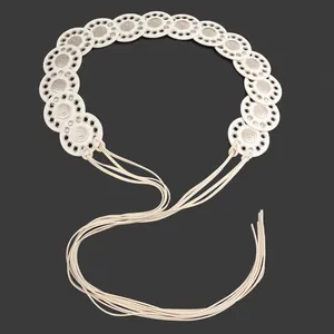 Close-up of white ethnic belt with ornate hollow-out metal discs and fringe straps.