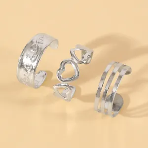 Close-up of three silver-colored open rings with heart and striped patterns