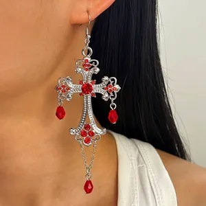 Primo piano di orecchino a croce gotica con strass rossi e pendenti a goccia di sangue.