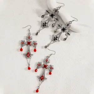Dettaglio degli orecchini a croce gotica con pietre preziose a goccia rosse e nere