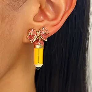 Nahaufnahme eines niedlichen Emaille-Bleistift-Ohrrings mit rosa Glitzerschleife am Ohr