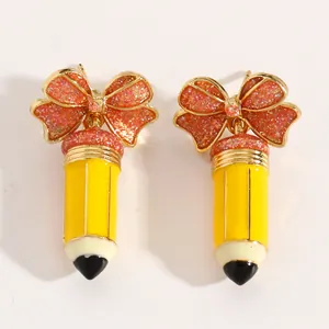 Makroansicht von gelben Emaille-Bleistift-Ohrringen mit glitzernden rosa Schleifen