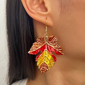 Close-up of a colorful maple leaf drop earring with autumn enamel texture