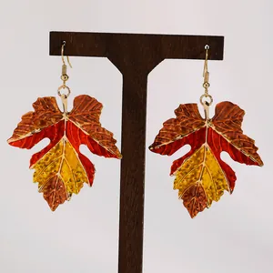 Detailed macro view of colorful enamel maple leaf earrings for autumn vibes.