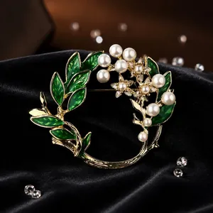 Nahaufnahme einer eleganten Kranzbrosche mit grünen Emaille-Blättern und Perlen.