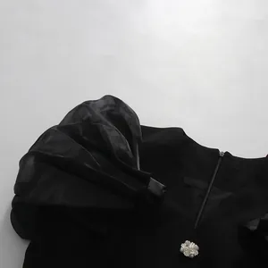 Close-up of black V-neck dress featuring pleated puff sleeves and a decorative crystal button