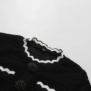 Primer plano del ribete blanco ondulado y botones decorados en vestido negro texturizado.