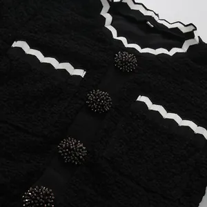 Detalle de un vestido negro de estilo francés con borde ondulado blanco y botones decorativos.