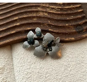 Detailansicht einer antiken silbernen Blumenbrosche mit dunklen Naturstein-Akzenten.