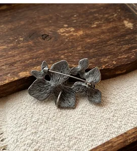 Detaillierte Rückansicht einer antiken silbernen Blumenbrosche mit Anstecknadel auf Stoff