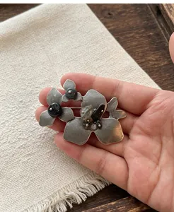 Nahaufnahme einer antiken silbernen Blumenbrosche mit dunklen Natursteinen in der Hand