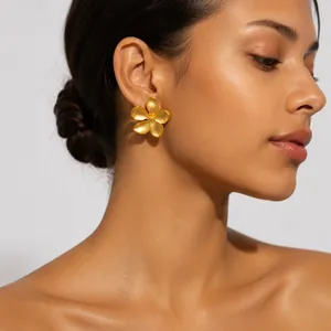 Elegant large matte gold plumeria flower stud earring worn by a model in a profile shot.