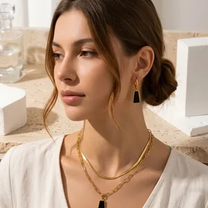 Modella indossa set di gioielli geometrici in acciaio al titanio nero e oro con orecchini.