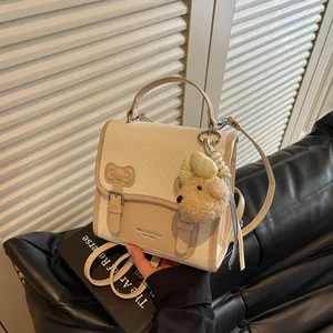 Detail view of a cream academy-style backpack featuring woven texture and a plush dog charm.