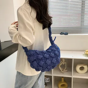 Blue quilted bubble crossbody cloud bag shown on model's shoulder in minimalist room setting.