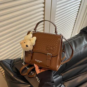 Close-up view of a brown preppy style backpack featuring a cute plush teddy bear charm