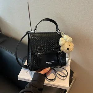 Detailed view of a black woven fashion backpack with a cute teddy bear charm accessory