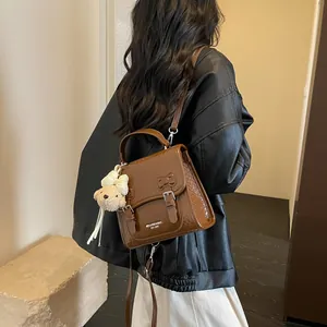 Detail view of a brown woven college style backpack being worn, featuring a cute bear charm