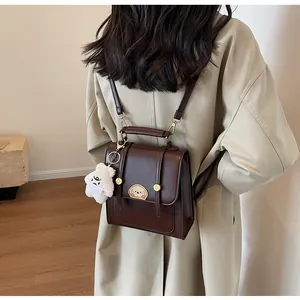 Vue détaillée d'un mini sac à dos marron en similicuir vintage porté sur un trench-coat beige.