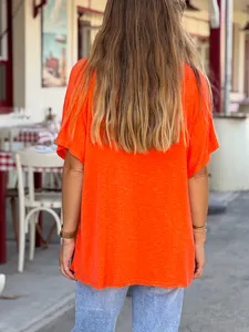 Back view of women's loose bright orange short sleeve t-shirt in casual outdoor setting