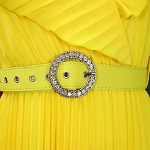 Detail of a bright yellow pleated dress with a sparkling rhinestone belt buckle.