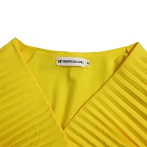 Detail shot of a bright yellow pleated V-neck maxi dress showing neckline and brand label