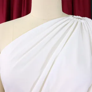 Detail of white one-shoulder jumpsuit showing pleated fabric and metal shoulder ring.