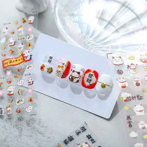 Vue détaillée d'autocollants 3D pour ongles Maneki-neko sur des faux ongles blancs.