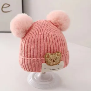 Close-up of pink baby knitted hat with dual pom-poms and cute teddy bear patch