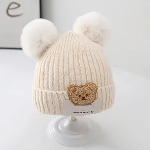 Close-up of soft cream knit baby beanie with cute bear patch and fluffy pom-poms