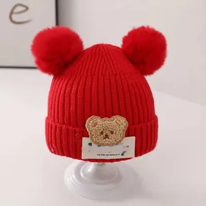 Red knitted baby winter hat featuring a cute bear patch and fluffy double pom-poms