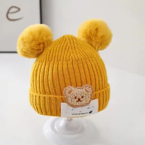 Close-up detail of yellow baby winter knit beanie with fluffy pom ears and bear patch