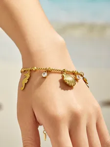 Gros plan d'un bracelet doré avec des pendentifs hippocampe et coquillage au poignet