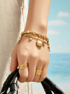 Détail d'un bracelet doré 18 carats avec breloques coquillage et bague fleurie sur main