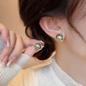 Detailed close-up of a model wearing vintage gold-framed grey pearl stud earrings