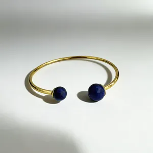 Detail view of an 18K gold plated stainless steel open bangle with blue lapis beads.
