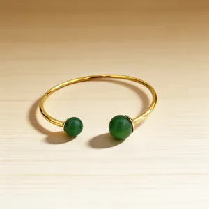 Detailed close-up of an 18K gold-plated cuff bracelet featuring green beads on wood