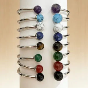 Detail of stainless steel open bangles with various colorful gemstone beads on a white stand