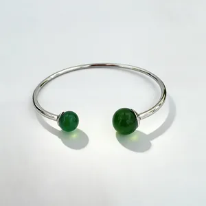 Detailed view of a silver stainless steel open bangle with two green gemstone beads on ends