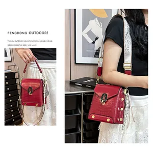 Dettaglio ravvicinato di una borsa rossa con motivo a coccodrillo e tracolla larga decorativa.