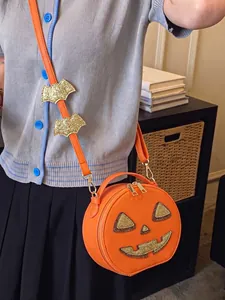 Detail view of the orange pumpkin crossbody bag with glittery bat wing strap decorations.