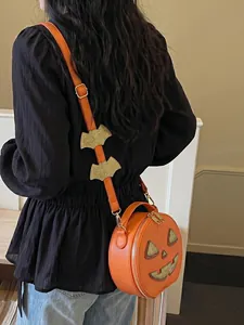 Orange pumpkin-shaped crossbody bag with bat-decorated strap shown on a female model