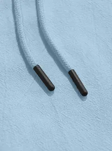 Close-up detail of light blue woven drawstrings and aglets on a linen hooded shirt texture