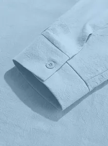 Close-up of light blue cotton linen shirt cuff showing button and textured fabric